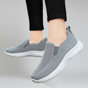 a lady foot wearing grey walking shoes on a plain background