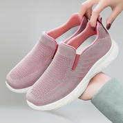 a lady holding a pair of pink walking shoes on a plain backgorund